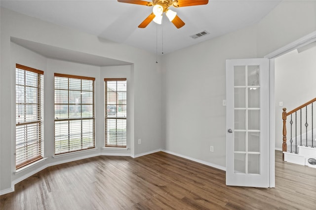 empty room with a wealth of natural light, visible vents, stairway, and wood finished floors