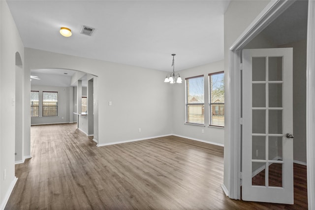 unfurnished dining area with arched walkways, a healthy amount of sunlight, visible vents, and wood finished floors