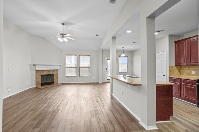 unfurnished living room with ceiling fan, a tile fireplace, a sink, baseboards, and dark wood-style floors