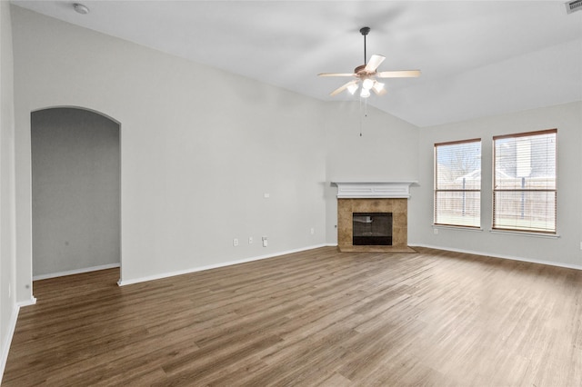 unfurnished living room featuring arched walkways, a fireplace, wood finished floors, a ceiling fan, and vaulted ceiling