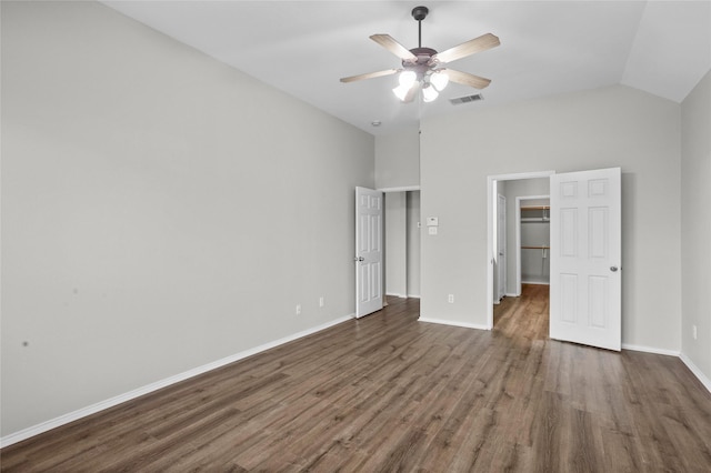 unfurnished bedroom featuring a walk in closet, baseboards, vaulted ceiling, and dark wood-style flooring