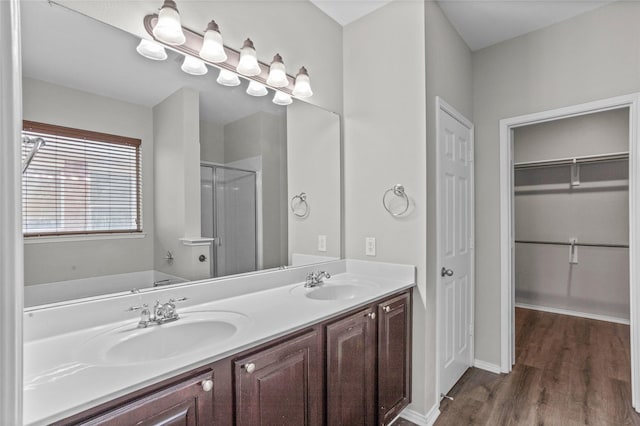 bathroom featuring a shower stall, a walk in closet, a sink, and wood finished floors