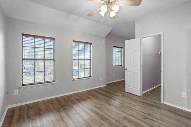 empty room with lofted ceiling, ceiling fan, baseboards, and wood finished floors