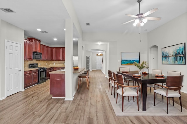 kitchen with arched walkways, light wood-style flooring, light countertops, reddish brown cabinets, and black appliances