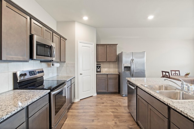 kitchen featuring stainless steel appliances, decorative backsplash, a sink, light stone countertops, and light wood-type flooring