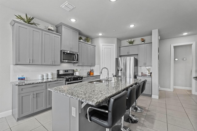 kitchen featuring an island with sink, light stone counters, a kitchen breakfast bar, stainless steel appliances, and a sink