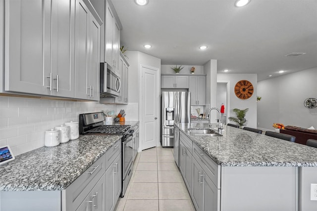 kitchen featuring light tile patterned floors, a kitchen island with sink, stainless steel appliances, a sink, and tasteful backsplash