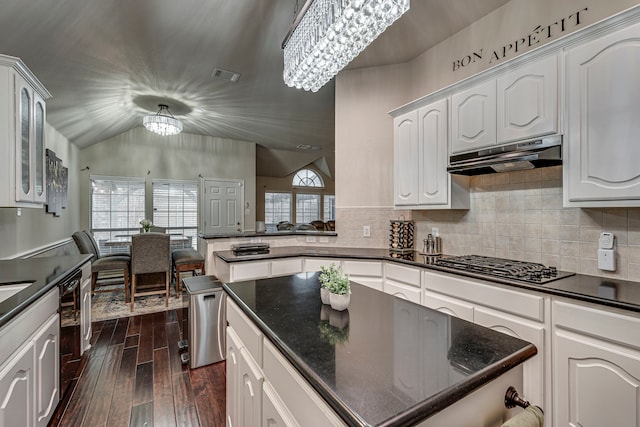 kitchen with under cabinet range hood, white cabinetry, dark countertops, glass insert cabinets, and an inviting chandelier