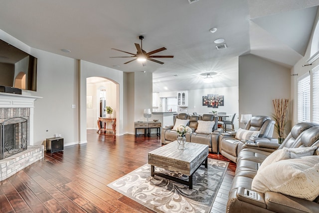 living area featuring baseboards, visible vents, arched walkways, dark wood-type flooring, and a brick fireplace