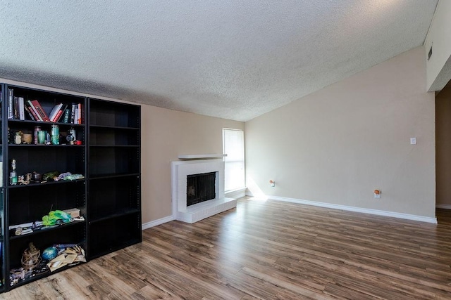 living area featuring a textured ceiling, a fireplace, wood finished floors, and baseboards