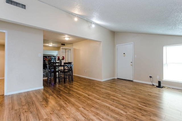 unfurnished dining area featuring visible vents, vaulted ceiling, a textured ceiling, and wood finished floors