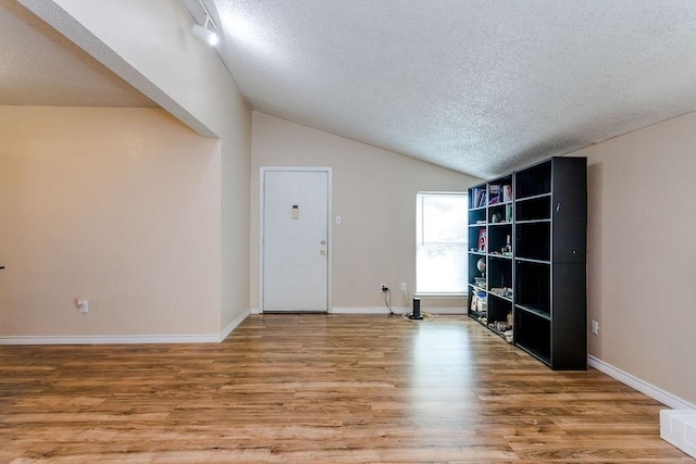 spare room featuring lofted ceiling, a textured ceiling, baseboards, and wood finished floors