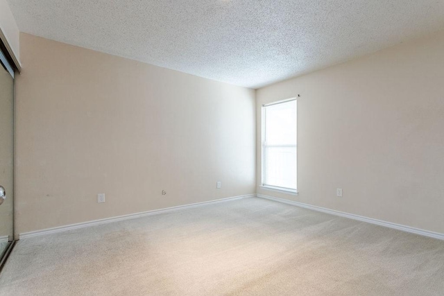 unfurnished room with light carpet, baseboards, and a textured ceiling