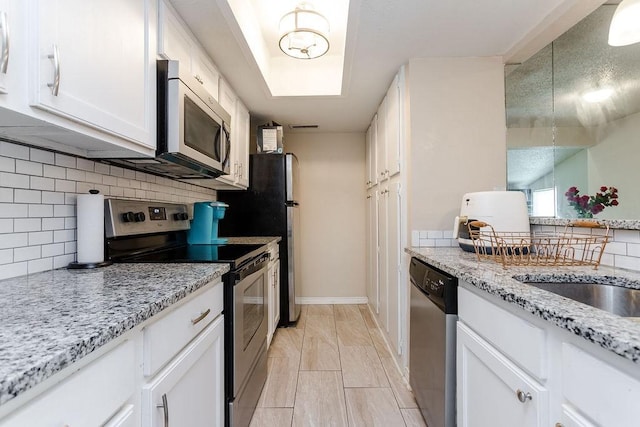 kitchen featuring stainless steel appliances, tasteful backsplash, white cabinetry, light stone countertops, and baseboards