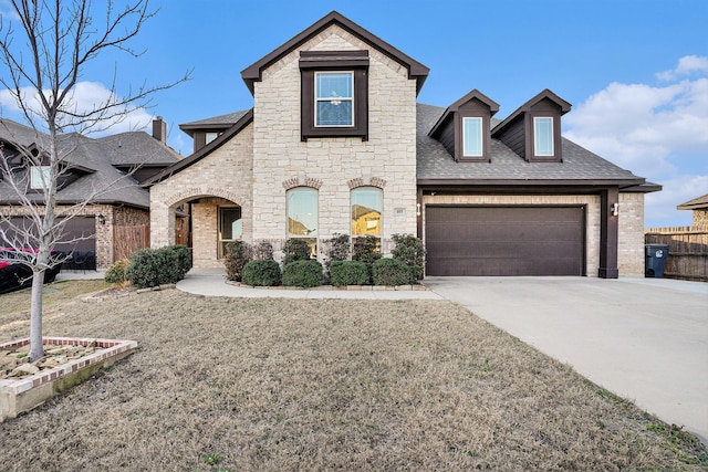 view of front of house with roof with shingles, concrete driveway, an attached garage, fence, and stone siding