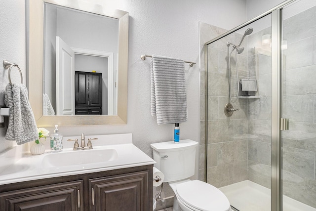 full bath featuring a textured wall, toilet, a shower stall, and vanity