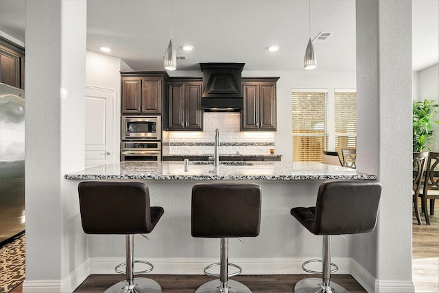 kitchen featuring light stone counters, stainless steel appliances, custom range hood, decorative backsplash, and a sink