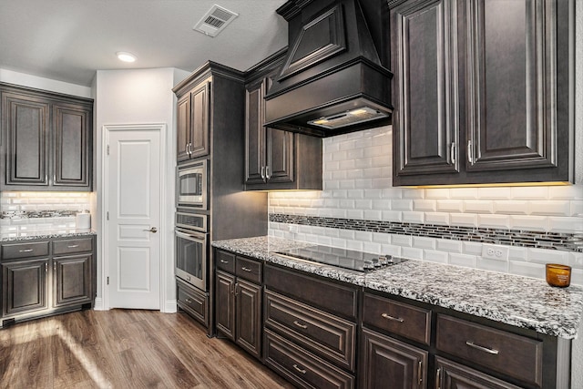 kitchen featuring stainless steel appliances, premium range hood, dark wood finished floors, and light stone counters