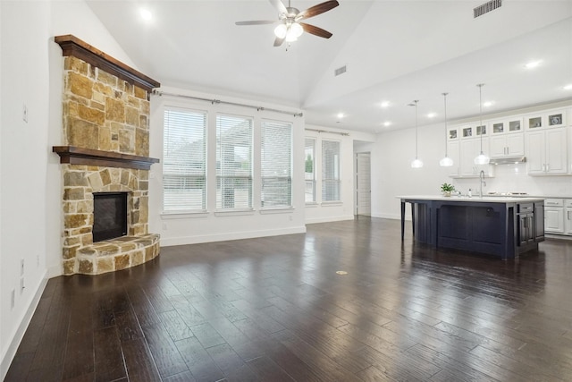 unfurnished living room featuring baseboards, visible vents, a ceiling fan, dark wood-type flooring, and a fireplace