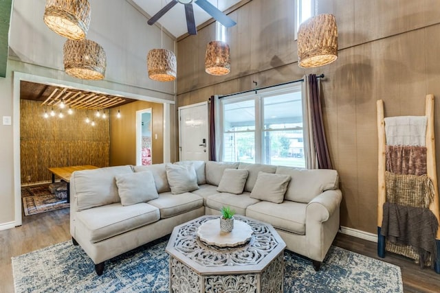 living room with ceiling fan, a high ceiling, baseboards, and wood finished floors