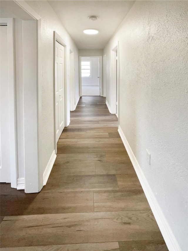 corridor featuring baseboards, dark wood-style flooring, and a textured wall