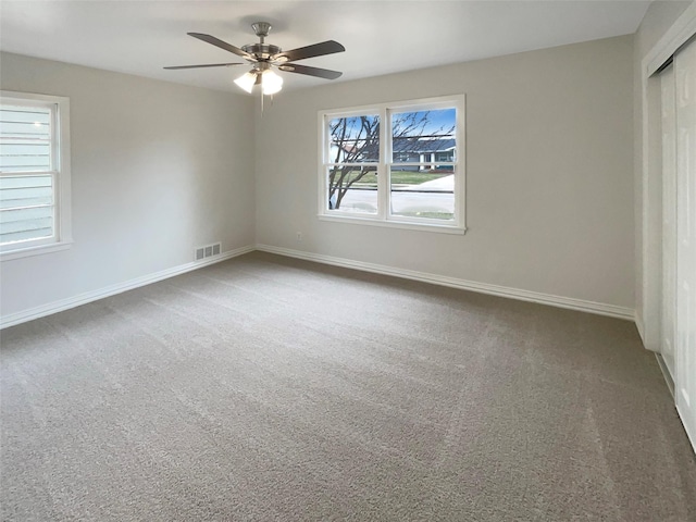 carpeted empty room featuring baseboards, visible vents, and a ceiling fan