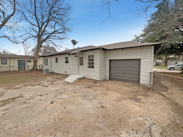 rear view of house with a garage, fence, dirt driveway, and central air condition unit