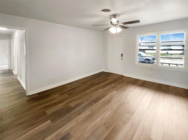 spare room with a ceiling fan, visible vents, dark wood finished floors, and baseboards