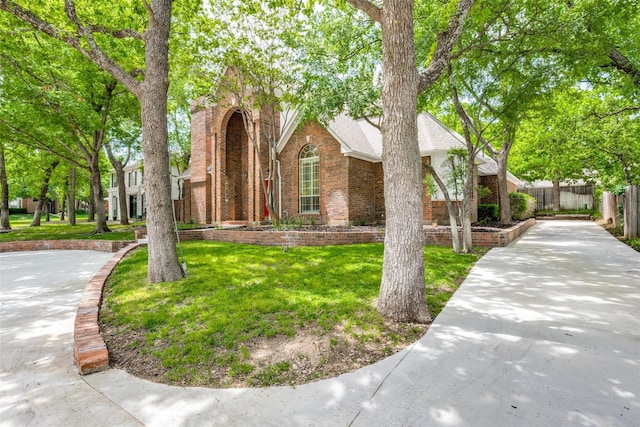 view of front of house featuring a shingled roof, fence, a front lawn, and brick siding