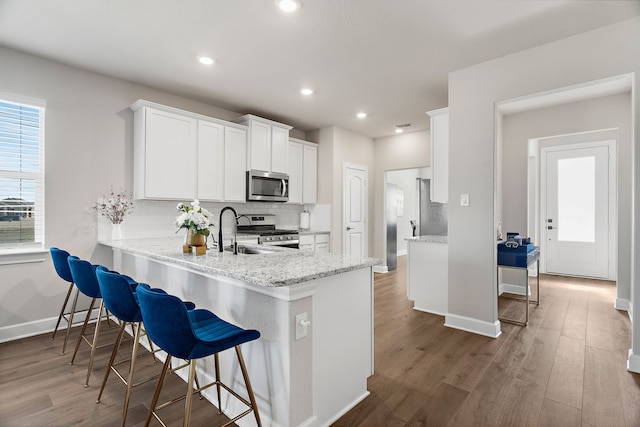 kitchen featuring white cabinets, appliances with stainless steel finishes, a peninsula, light stone countertops, and backsplash