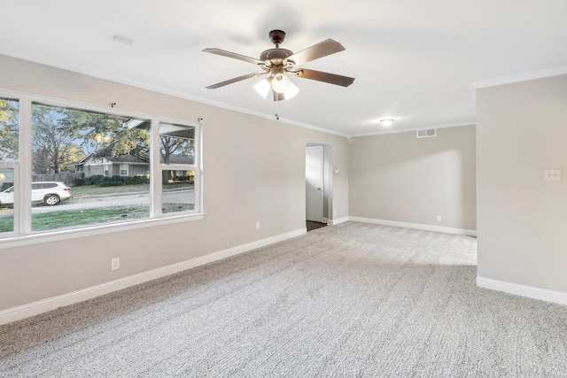 carpeted empty room featuring a ceiling fan, visible vents, crown molding, and baseboards