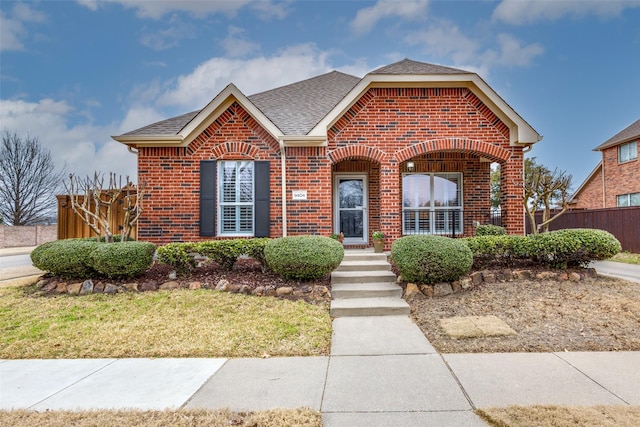 view of front of house with a shingled roof, brick siding, and fence