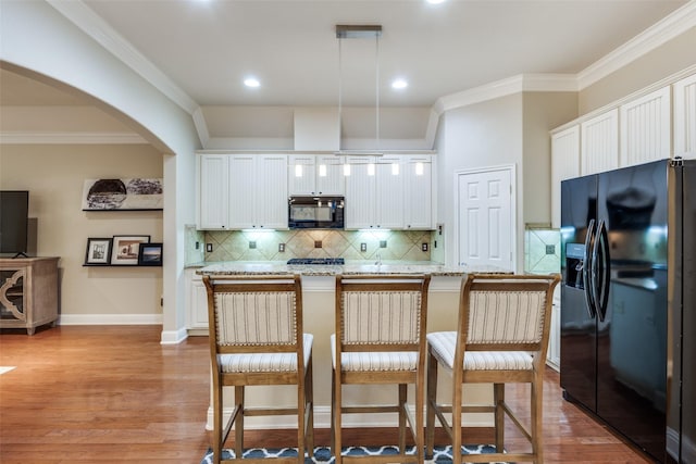 kitchen featuring arched walkways, white cabinetry, hanging light fixtures, black appliances, and an island with sink