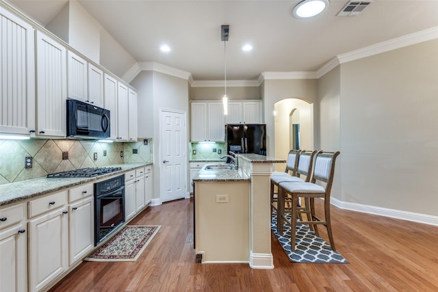 kitchen with visible vents, white cabinets, hanging light fixtures, black appliances, and a center island with sink