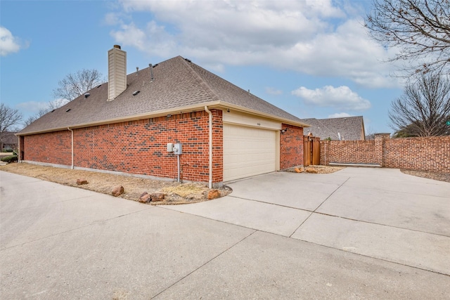 view of side of property with brick siding, a chimney, a shingled roof, fence, and driveway