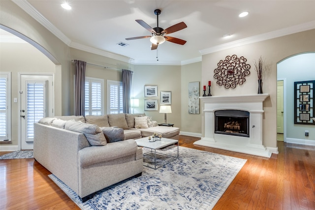 living room featuring arched walkways, crown molding, a fireplace with raised hearth, wood finished floors, and baseboards