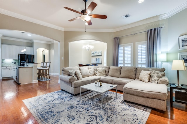 living room featuring arched walkways, wood finished floors, visible vents, and crown molding