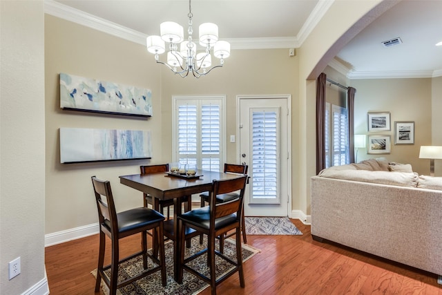 dining room featuring arched walkways, wood finished floors, visible vents, and crown molding