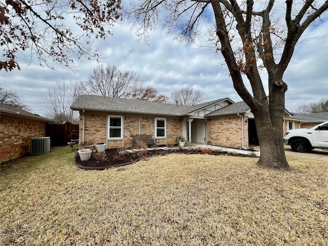 single story home featuring a shingled roof, cooling unit, brick siding, and a front yard