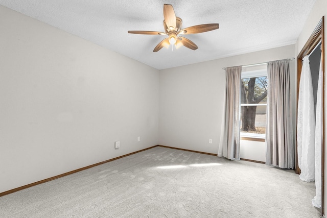 spare room featuring light carpet, ceiling fan, baseboards, and a textured ceiling