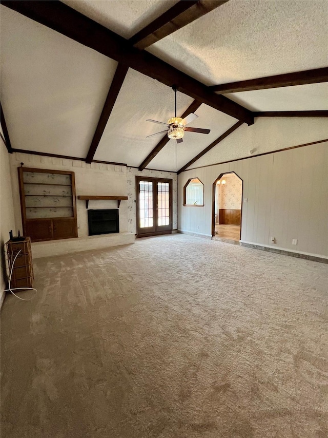 unfurnished living room featuring arched walkways, ceiling fan, vaulted ceiling with beams, a textured ceiling, and carpet floors