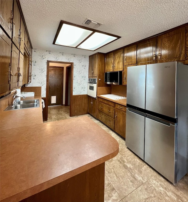 kitchen with stainless steel appliances, visible vents, wainscoting, a sink, and wallpapered walls