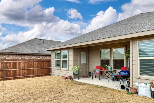 rear view of property featuring a yard, a patio area, fence, and a shingled roof