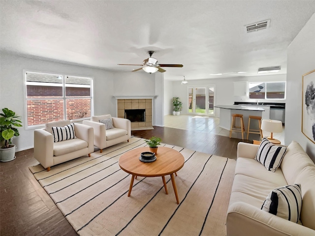 living area featuring baseboards, visible vents, a ceiling fan, a tiled fireplace, and wood finished floors