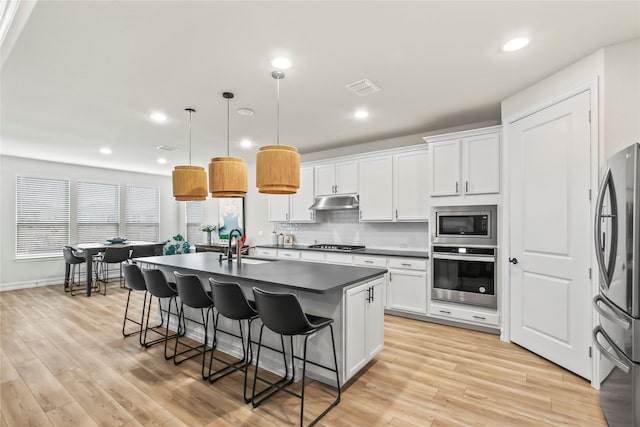 kitchen with stainless steel appliances, a sink, white cabinets, an island with sink, and pendant lighting