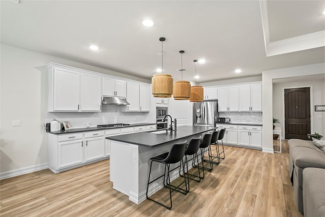 kitchen with white cabinets, dark countertops, a kitchen breakfast bar, hanging light fixtures, and under cabinet range hood