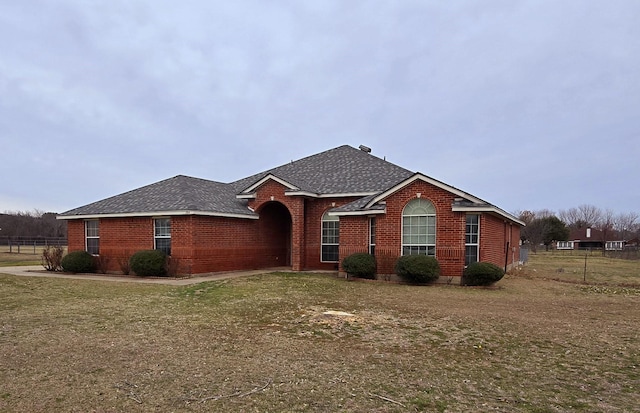 ranch-style home featuring brick siding, a front lawn, a shingled roof, and fence