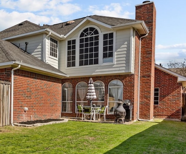 rear view of house featuring brick siding, a chimney, and a yard