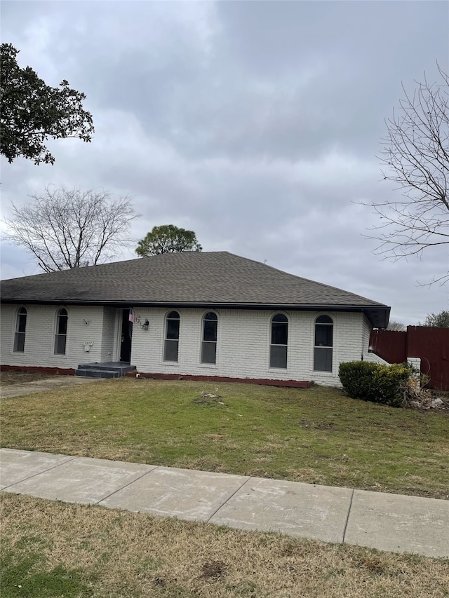 view of front of property with brick siding, roof with shingles, fence, and a front yard