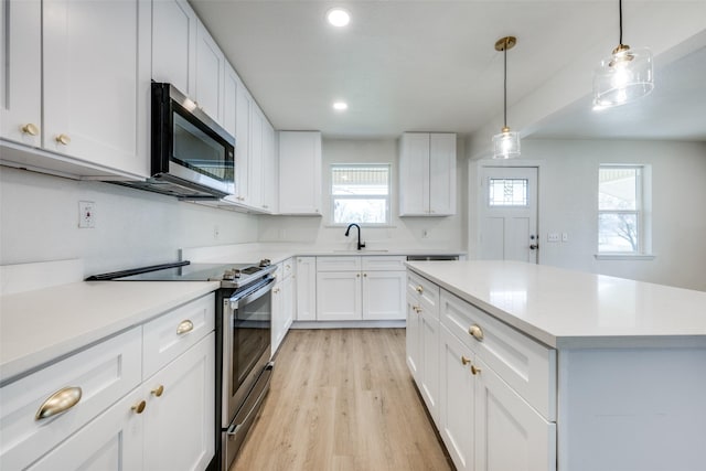 kitchen with a sink, white cabinetry, light countertops, appliances with stainless steel finishes, and hanging light fixtures